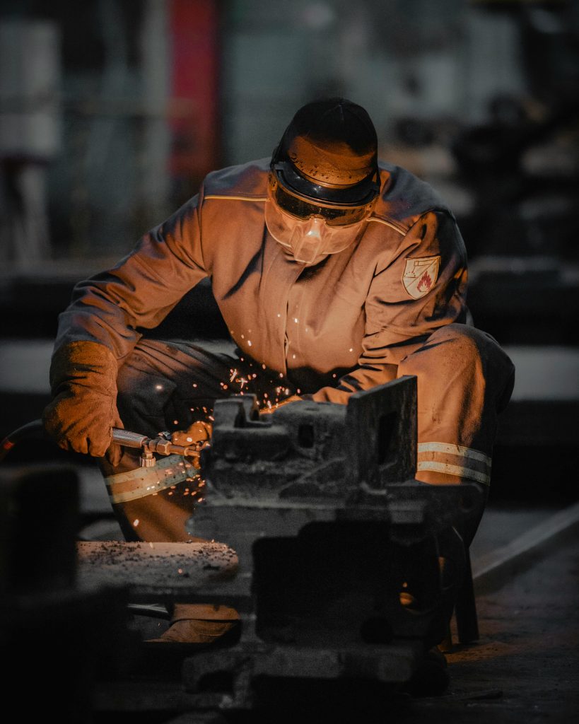Welder in protective gear working with sparks in an industrial workshop.